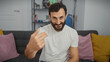 © Krakenimages.com - Middle-aged bearded man in a white shirt gestures invitingly in his modern living room.