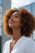 © olegganko - Woman with curly hair gazes upward in a cityscape under a bright sky during the day
