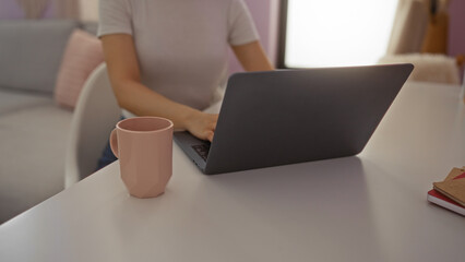 Young woman using laptop at home office with coffee cup on desk in cozy living room setting