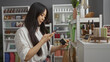 © Krakenimages.com - Young woman taking a photo of a product with her mobile phone in an indoor home decor store in china, surrounded by various decorative items