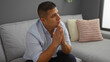 © Krakenimages.com - Young hispanic man sitting indoors deep in thought in his living room home