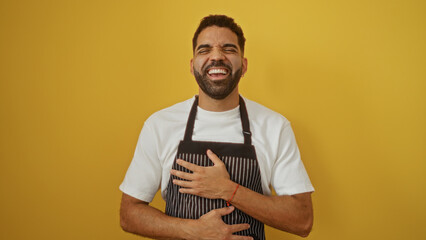 Handsome man laughing joyfully in front of a bright yellow background wearing a striped apron and white shirt