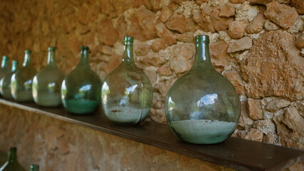 Wall Mural - Rustic glass bottles neatly arranged on a shelf against a textured stone wall in an indoor setting create a vintage, nostalgic atmosphere.