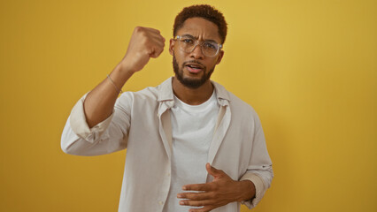 Young, african, american, man standing isolated over yellow background with a serious expression and raised hand in a confident and assertive gesture.