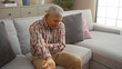 © Krakenimages.com - Grey-haired hispanic man sitting on a couch in his living room at home, holding his elbow in pain and showing discomfort.