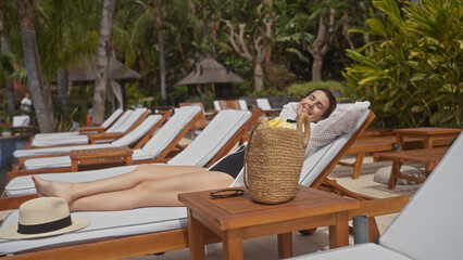 Poster - Hispanic woman relaxing at bali resort poolside, vacation tranquility with sunhat and tropical setting.