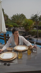 Poster - A young woman dining alone at a luxurious resort terrace in bali, contemplating a tranquil outdoor setting.