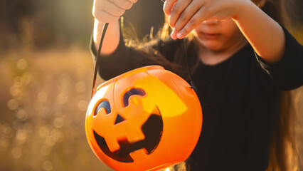 Close-up portrait of a 4-5 year old girl in a witch costume with a candy bucket against a background of autumn leaves. Copy space.