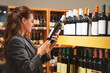 © Barillo_Images - Woman holding a wine bottle and reading the label while standing in a wine store.