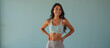© Roman - A smiling, fit young Asian woman with long dark hair, wearing a light green sports bra and matching shorts, stands confidently with hands on her hips against a light green background.