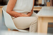© peopleimages.com - Business woman, hands and stomach ache with pain, digestion or sore gut on chair at office. Closeup, female person or employee with gastro, reflux or abdominal cramps for period or menstrual cycle