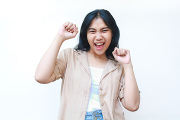 happy asian woman celebrate victory with raised fist wearing casual brown clothes isolated on white background