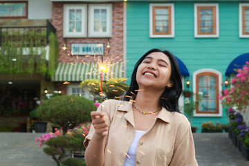 portrait of beautiful happy young asian woman holding sparklers fireworks to celebrate new year eve with garden party standing in outdoor vintage house yard