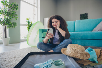 Photo of young tired woman wearing casual outfit preparing clothes for weekend vacation trip sit floor indoors loft modern house