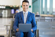 © Minerva Studio - Smiling businessman working on laptop at airport