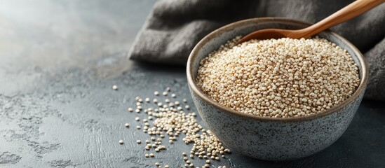 Leinwandbilder - A bowl of uncooked dry white quinoa seeds with a spoon on a gray table viewed up close. with copy space image. Place for adding text or design