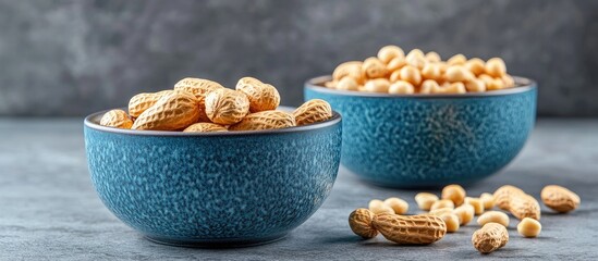 Poster - Two blue ceramic bowls contain nuts One bowl has peanuts in their shells while the other holds peeled nuts Beside the bowls are peeled peanut kernels set against a gray background Closeup