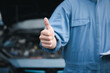 © sorapop - Asian mechanic smiles showing thumbs up while repairing a car. Skilled technician's expertise in vehicle maintenance ensures quality service and safety in the garage.