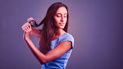 Young woman brushing long hair on purple background