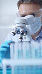 Man scientist with protective glasses, mask and gloves is using microscope in laboratory, vertical portrait of researcher. Microbiology and science