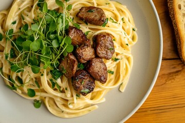 Close-up of a plate of creamy pasta with sauteed meat and microgreens, garnished with parsley.