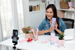 © Summit Art Creations - Young beautiful Asian girl reviewing moisturizing body lotion cream product to make glow skin testing on arm on social media online live recording smartphone with bestseller at modern room. Stratagem.