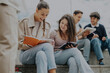 © qunica.com - A diverse group of students study together outside, discussing ideas with a professor offering guidance. The scene represents teamwork, education, and collaboration in a casual setting.