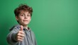 © Yury - Young boy with confident smile giving thumbs up against green background with copy space