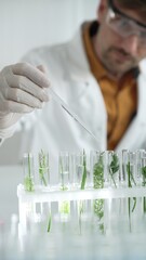 Man scientist wearing a lab coat, white gloves and protective glasses, is dripping liquid from a pipette into a test tube with a green plant inside, vertical close up view. Science and medicine