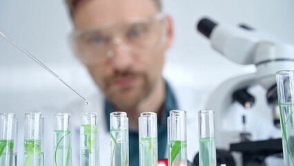 Man researcher with safety glasses is working with lab tubes using a pipette in laboratory, close-up of lab equipment. Science and medicine