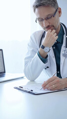 Wall Mural - Doctor and a patient. The physician, wearing a white medical coat over a green shirt, gesturing with his hands during a consultation in the clinic. Medicine concept