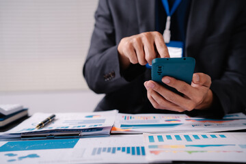 Wall Mural - businessman sits at his office desk, analyzing financial documents and graphs on his laptop. paperwork, calculator, and charts, he strategizes investments, audits, tax planning for success.