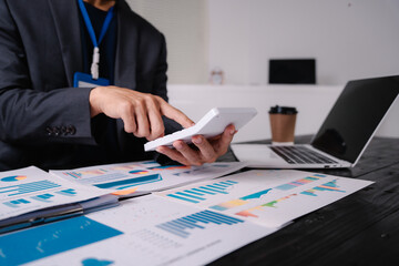 Wall Mural - businessman sits at his office desk, analyzing financial documents and graphs on his laptop. paperwork, calculator, and charts, he strategizes investments, audits, tax planning for success.