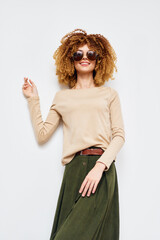 Fashion model with curly hair wearing sunglasses and a beige top poses against a simple white background, showcasing a stylish and confident look in casual attire