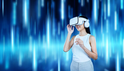 Female standing and wearing white VR headset and white sleeveless connecting metaverse, future technology creating cyberspace community. She enjoy looking fantasy blue light around her. Hallucination.