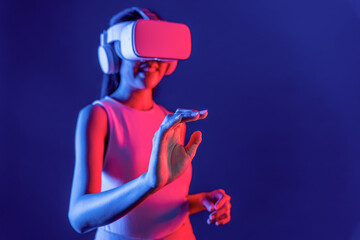 Smart female standing with surrounded by cyberpunk neon light wear VR headset connecting metaverse, futuristic cyberspace community technology. Woman using hand touching virtual object. Hallucination.