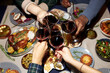 © Seventyfour - High angle shot of people clinking wine glasses celebrating Christmas together while sitting at dining table set with festive dishes during friends gathering at home party, camera flash