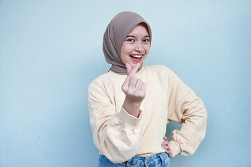 Young Asian Muslim woman in cream sweater and hijab making Korean heart love shape gesture with hands and fingers in various pose, isolated on gray background.