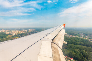 View of airplane wing, blue skies and green land during landing. Airplane window view.