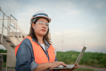 A female engineer   wearing a safety vest and a hard hat is using a laptop. She is focused on her work and she is in a serious mood