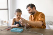 © fizkes - Positive loving Latin father and little girl making decoration from strings and beads together, developing manual skills in game. Caring middle aged dad enjoying handmade activity with cute daughter