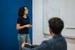 © qunica.com - A student stands in front of a classroom whiteboard, presenting data analysis to the class. Engaged in learning, the student explains the graph's significance to a peer.