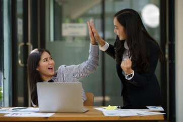 Two Asian woman colleagues give each other a high five, Successful business team working together concept.