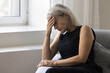 © fizkes - Tired depressed older woman pensioner hold hand on forehead feel headache weakness anxiety psychological discomfort. Stressed nervous aged female sit on couch with eyes closed get sudden panic attack