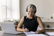 © fizkes - Diligent mature female in earphones remote student of third age university engaged in e-learning listen to video lecture on laptop take notes. Elderly employee upgrade professional skills study online