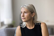 © fizkes - Head shot calm thoughtful aged lady sit on couch at home look aside ponder reflect create daily plans. Serious senior Caucasian female think about future concerned with idea lost in memories thoughts