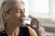 © fizkes - Smiling face of elderly lady relieving stress having glass of natural cold filtered water in dry hot summer day. Mature woman has healthy habit for easy skin body care hydrating drink enjoy every sip