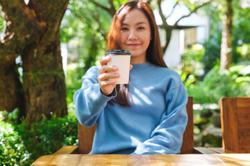 Poster - Portrait image of a woman holding and serving a cup of hot coffee in the outdoors cafe