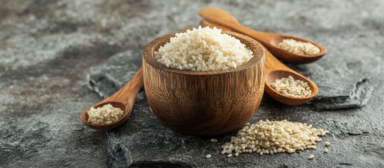 Canvas Print - Parboiled rice in a wooden cup accompanied by wooden spoons and grains beside it all arranged on a stone surface with copy space available