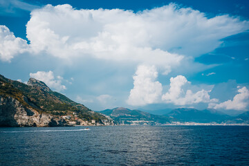 Panoramic view of Amalfi Coast from the sea with clear blue sky, mountains, and coastal buildings. Sunny summer day showcasing scenic landscape, cliffs, and tranquil Mediterranean waters..